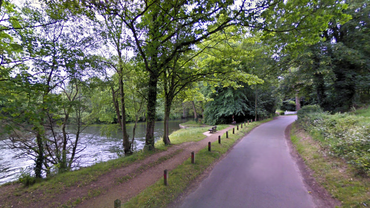 A wooded area around Horstead Mill, showing a narrow road and a footpath running along the edge of a waterway