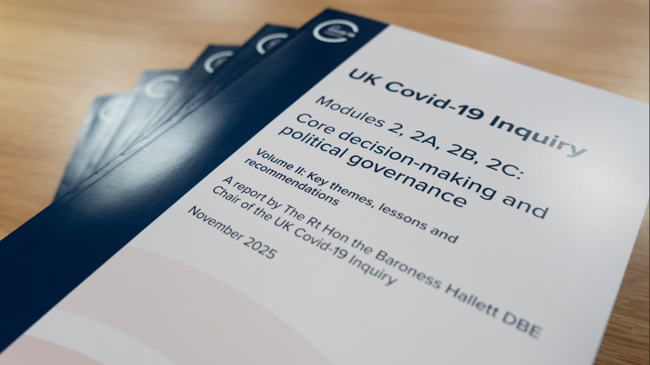 A pile of paper copies of the Covid inquiry module two report on a plain wooden desk