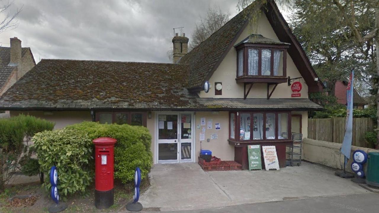 A view of the Post Office in Foxton. The small building has brown bay windows and a red post box outside.