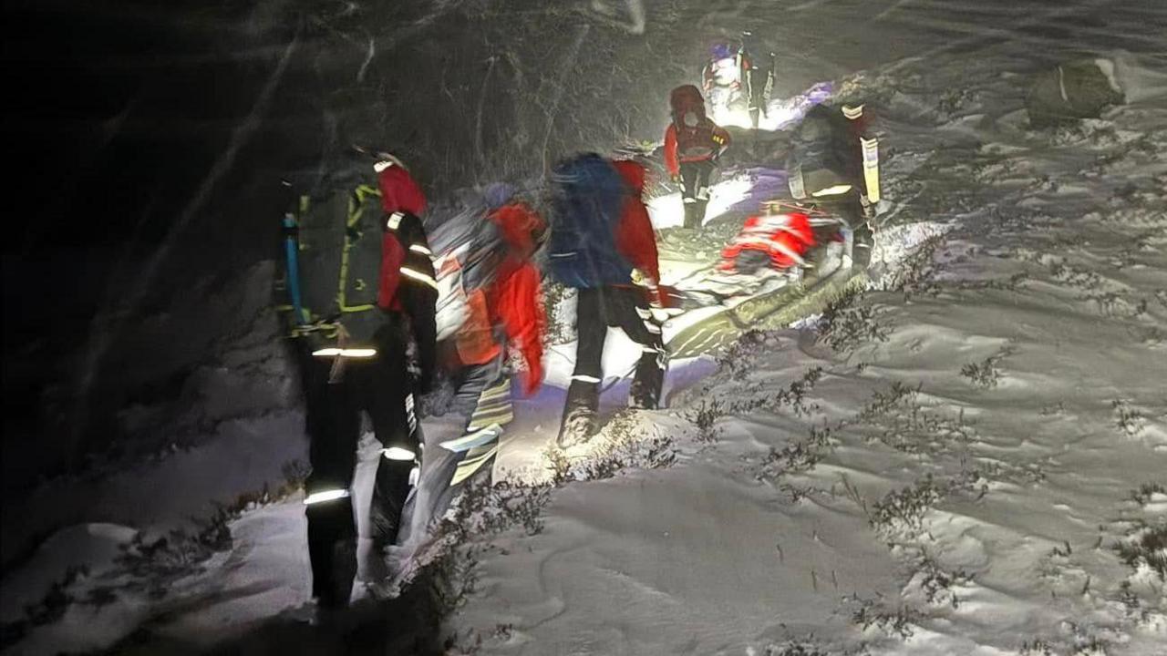 Members of a mountain rescue team wearing hi-vis and mountaineering clothing battle through thick white snow.