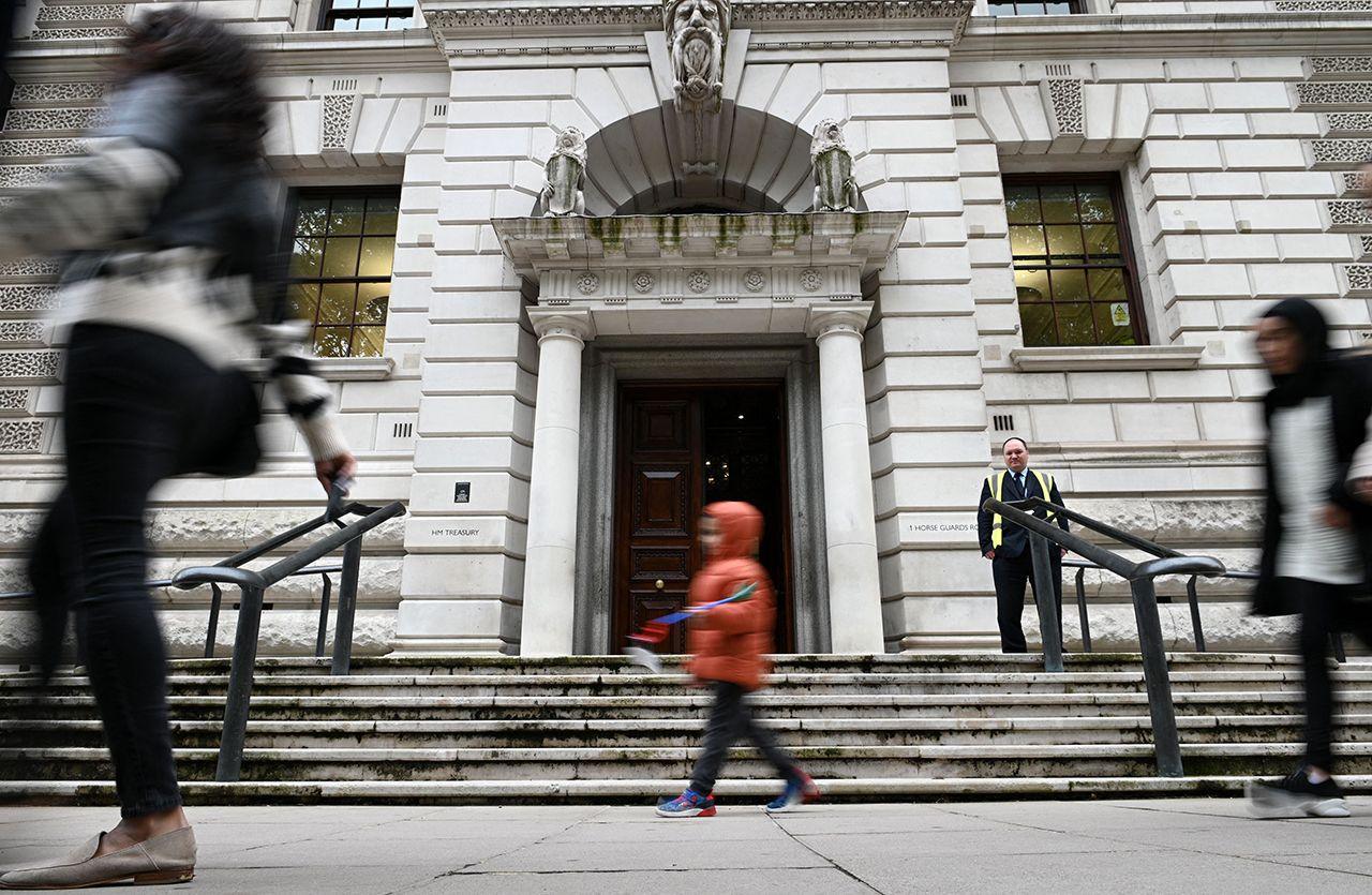 The entrance to the HM Treasury building in London is pictured in a front-on  shot with a security guard standing watch while pedestrians walk past, taked in London in October 2021