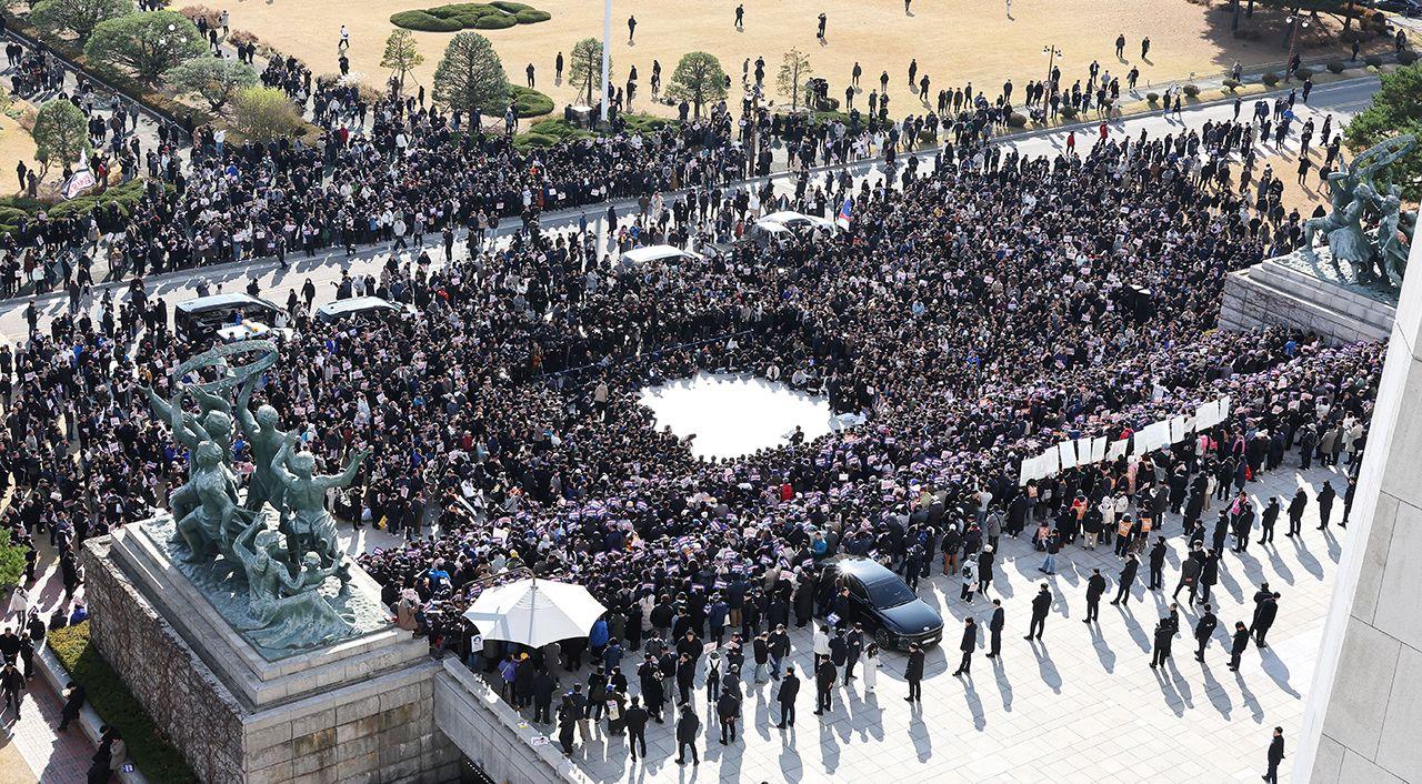 A wide shot showing a mass of people gathered in the National Assembly square in front of parliamentary statues, in Seoul on Wednesday