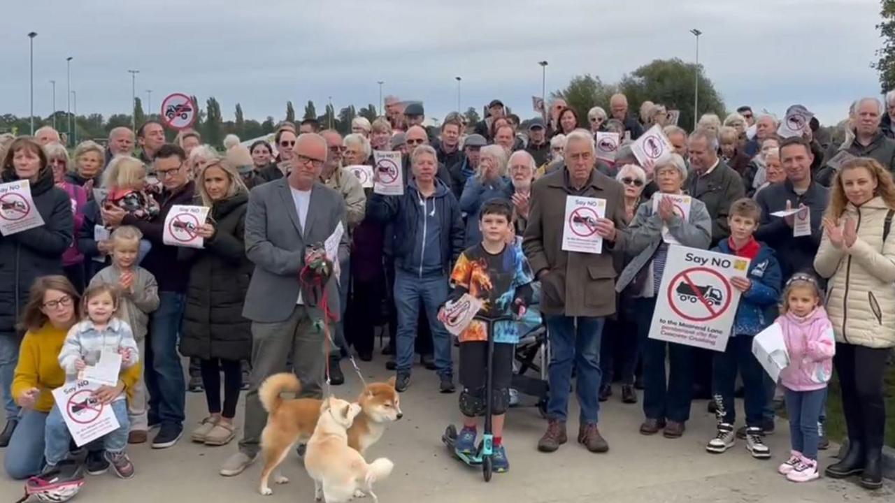 A group of campaigners clapping and holding signs against the formerly proposed concrete crushing plant. Children and dogs are also present. It's an overcast day.