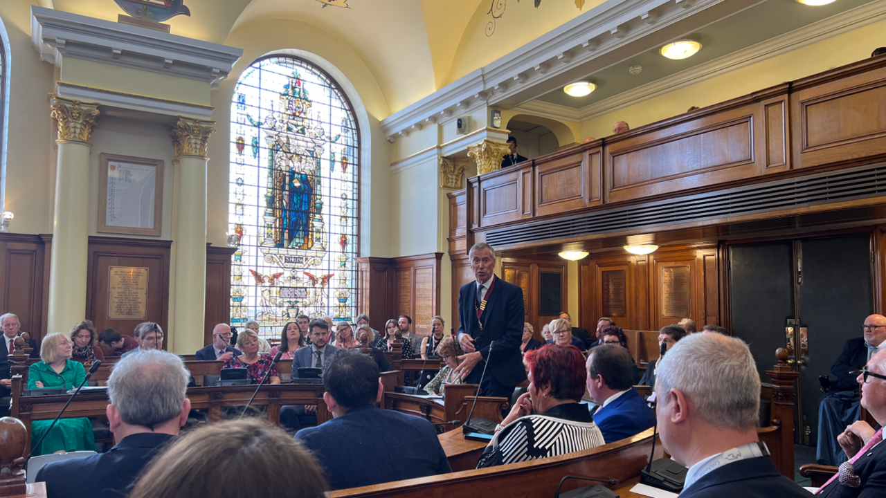 Council leader standing up in an ornate Colchester town hall council chamber addressing councillors.