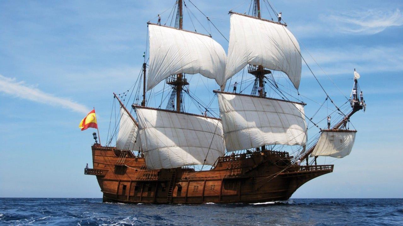 A replica of a 17th-century Spanish merchant ship sailing on the ocean at full sail with the Spanish flag flying 