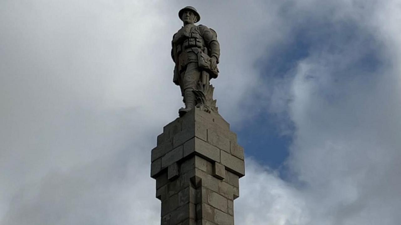 A statue depicting an infantry soldier on top of the Douglas war memorial, which made of grey stone.