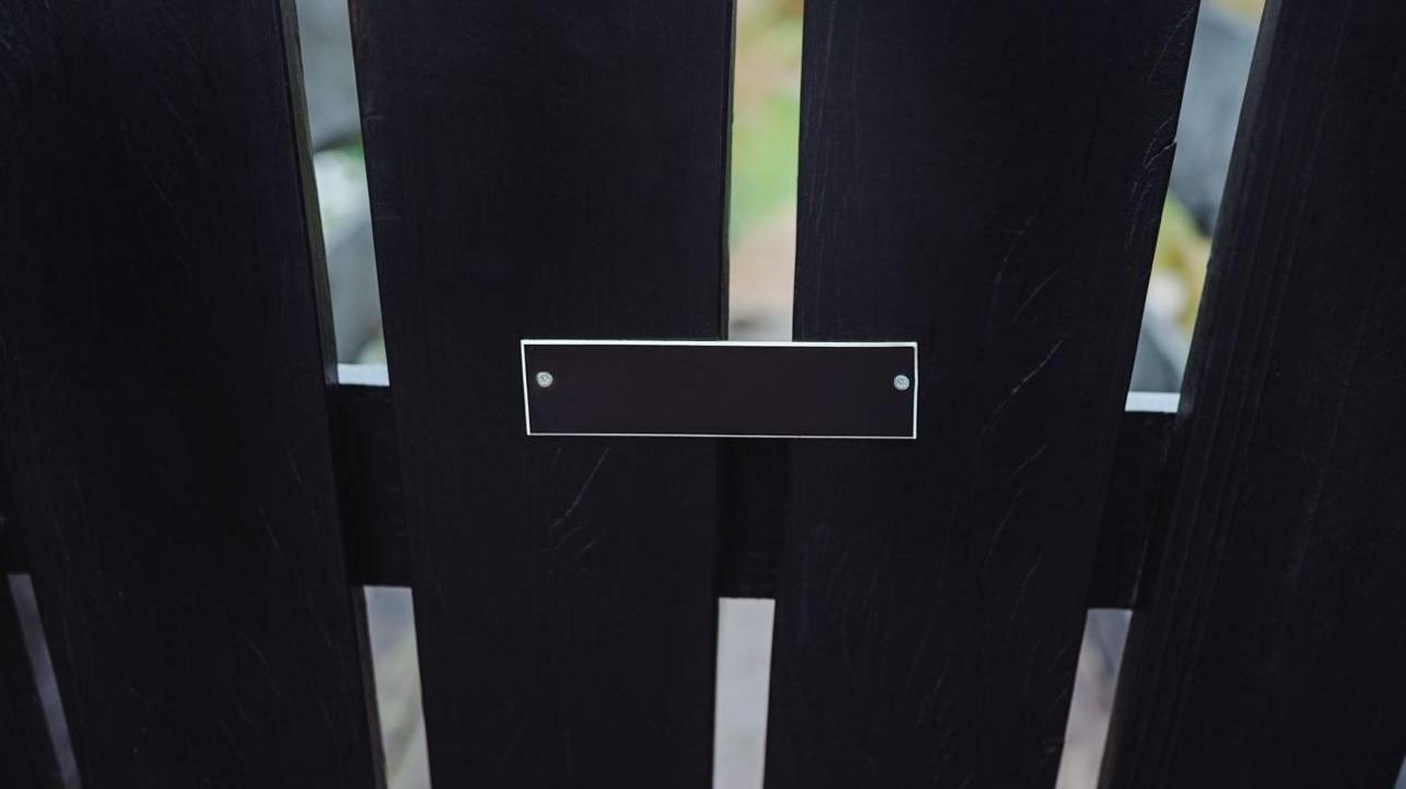 Black wooden fence with attached metal plate without inscription. Close-up photo, textured wood and simplicity of design.