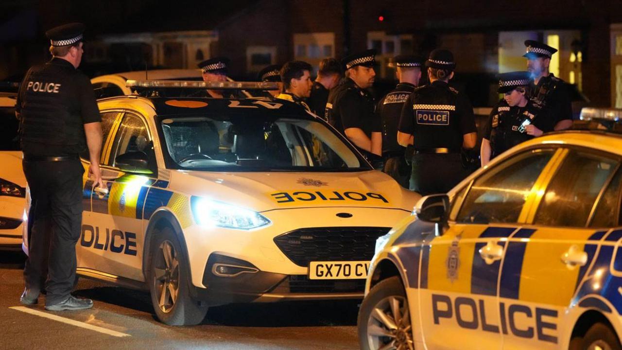 A large group of police officers stood next to police cars. 