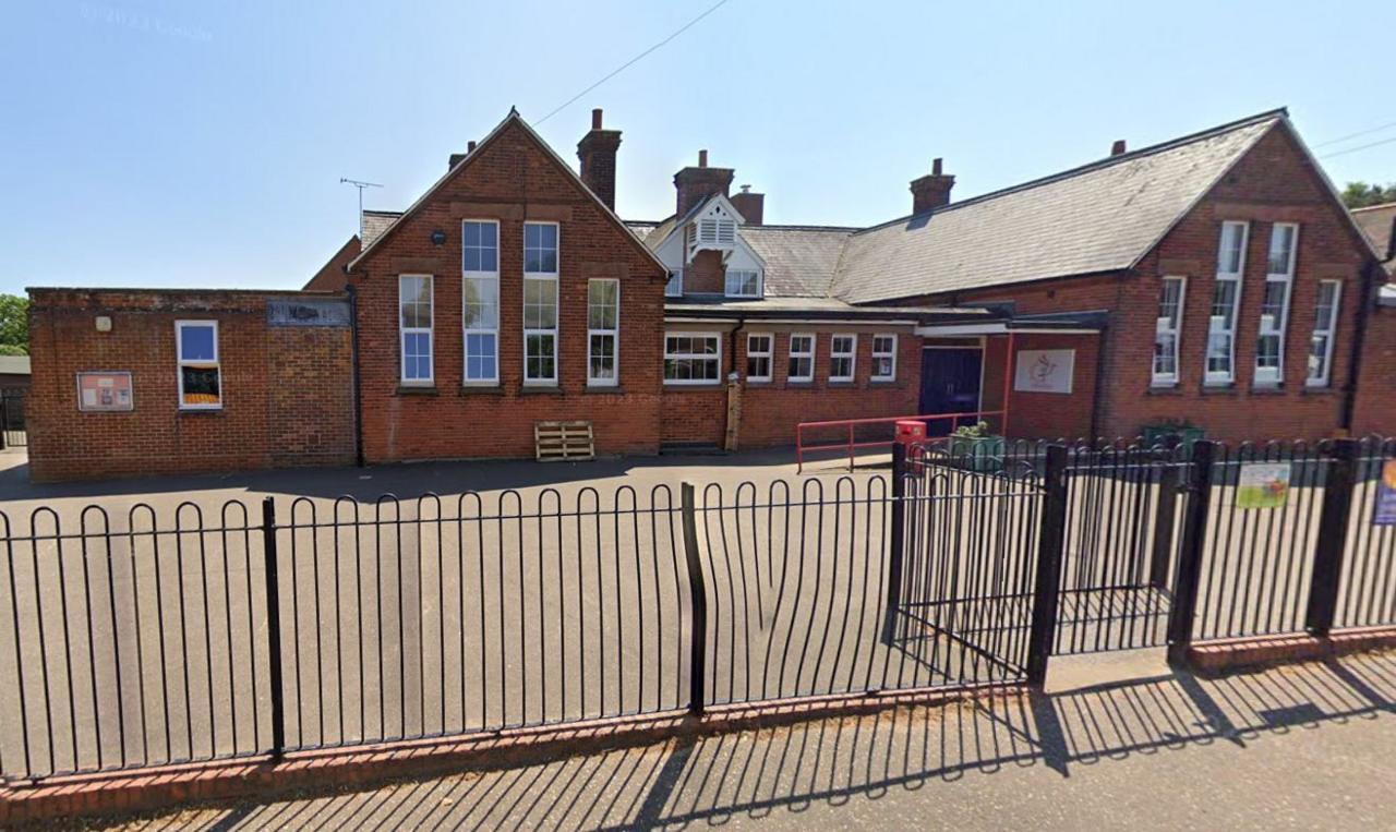 External view of Reepham Primary School with its playground visible behind a black metal fence. It is a sunny day.