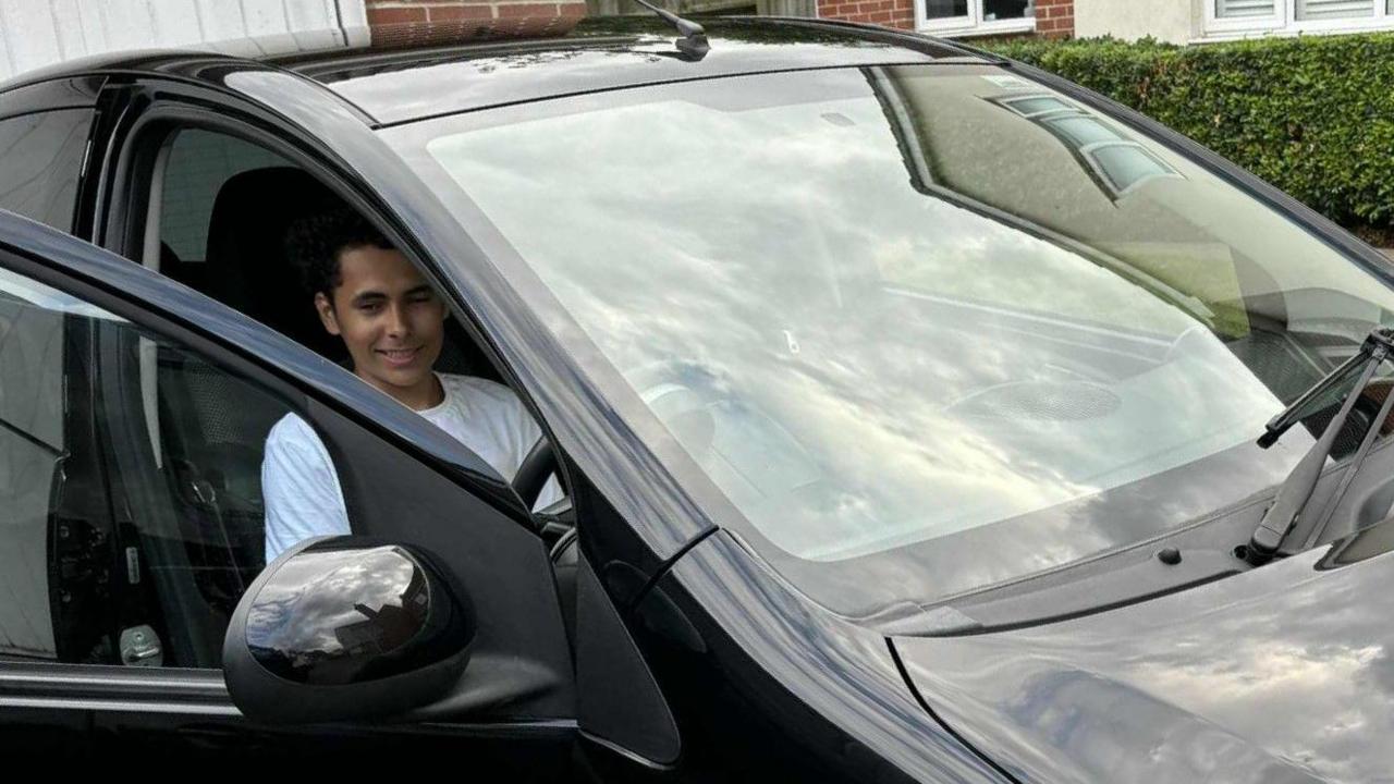Toby Newton sitting in the driver's seat of a black car. His door is open and he is looking towards the camera, although his eyes are slightly closed.