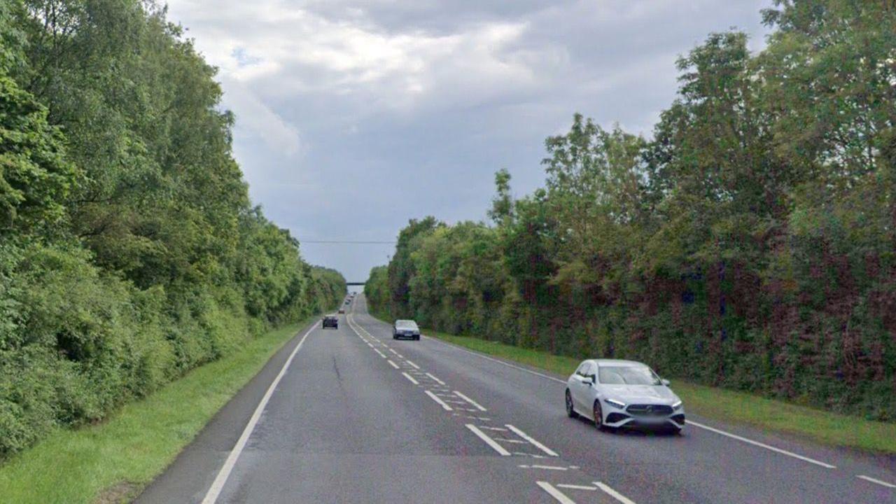 A street view image of the A46 carriageway. There are multiple cars driving on either side of the road with greenery on both verges