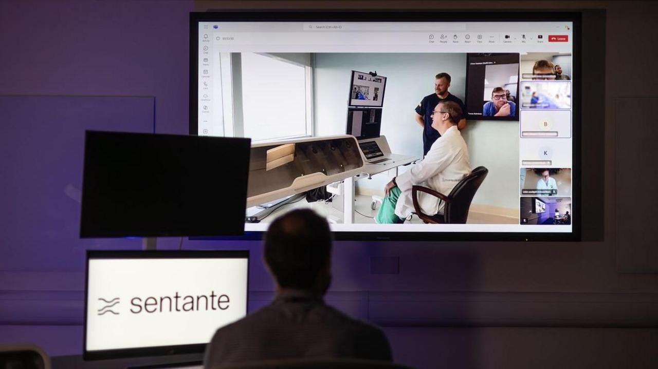 A man watches a big screen, where a medic is carrying out a procedure.