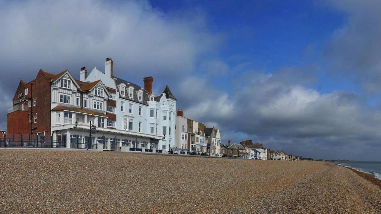 A view of Aldeburgh's seafront. Buildings of varying colours and shapes can be seen extending along the coastline behind the beach.