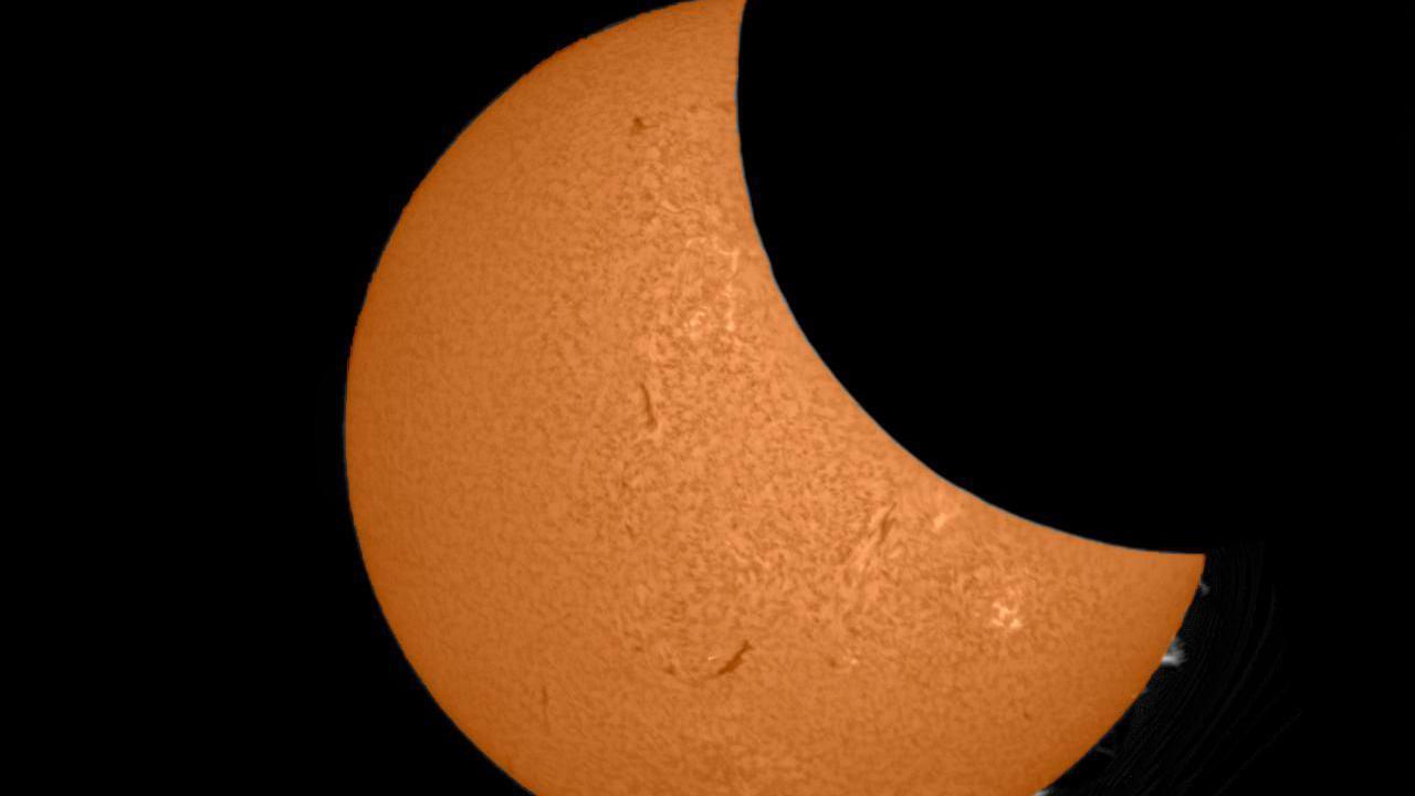 Partial eclipse, with about a third of a bright orange Sun covered