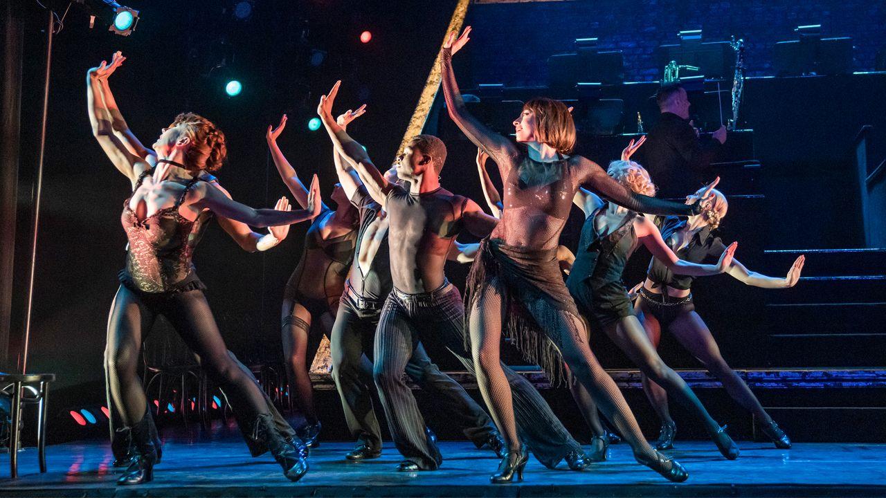 Dancers on stage dressed in black during Chicago. They all have their arms out stretched in a dance