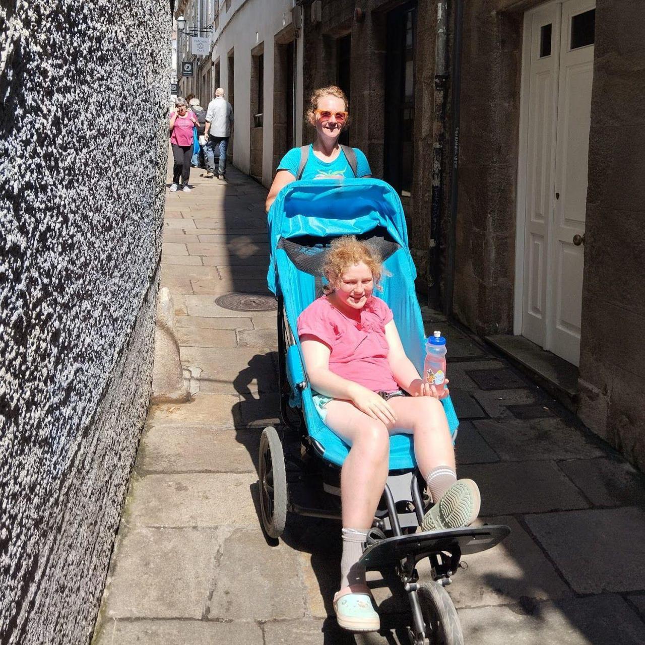 A woman pushed a teenage girl in a buggy down a narrow Spanish alley.