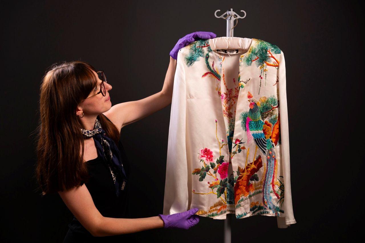 A curator holds up a white silk top with embroidered flowers