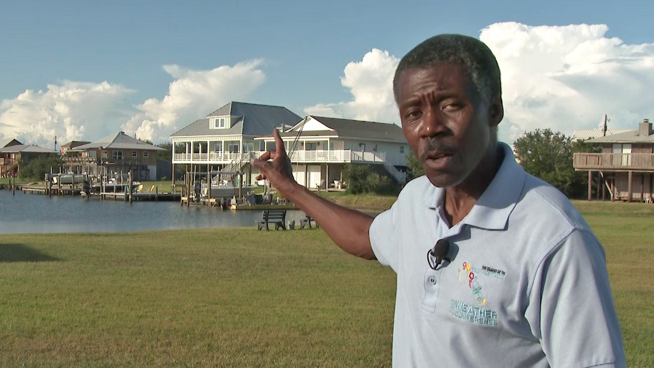 Alan Sealls wearing a blue t-shirt points at a waterfront property