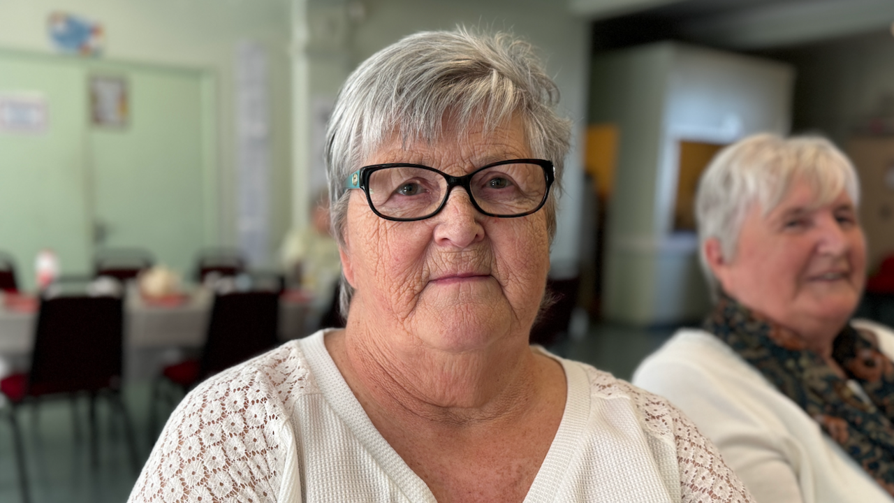 Denise wearing a white vest with black rimmed glasses is looking directly at the camera.