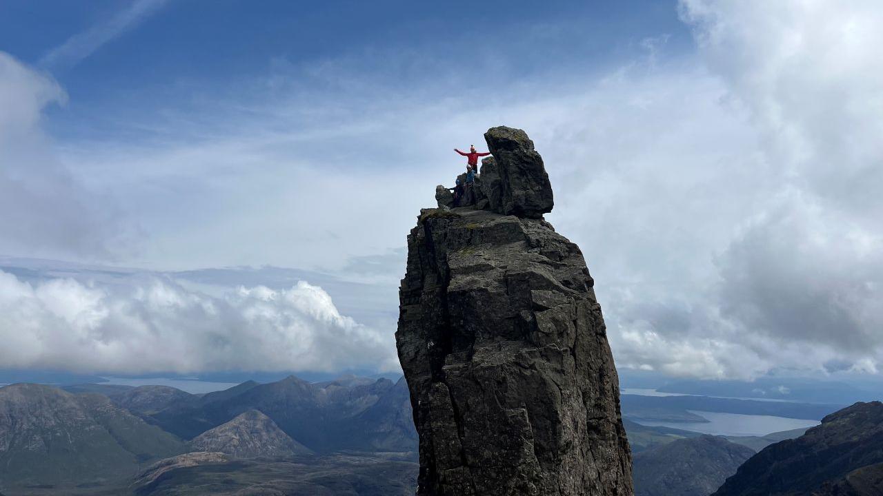 Three people on the pinnacle of a fin of rock with hills and valleys in the background