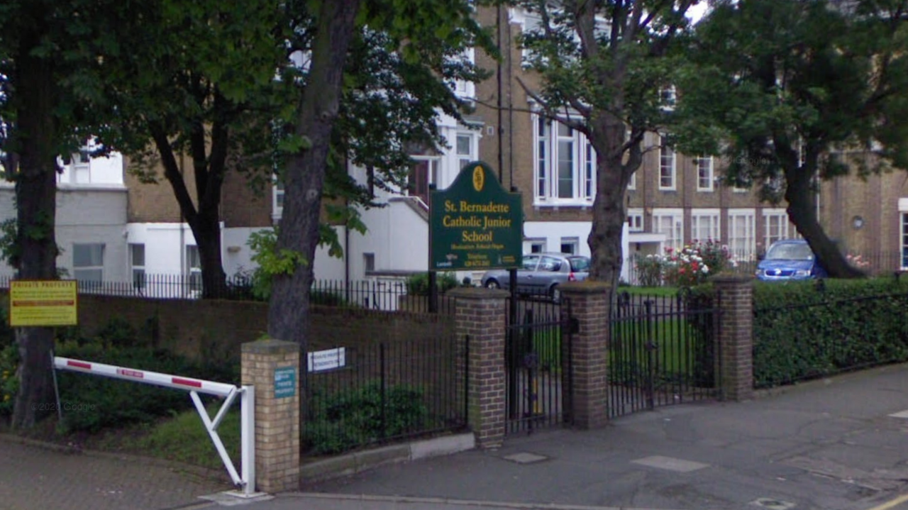 A Google street view showing the front of St Bernadette's school, showing the school gates, some trees and a pathway, as well as the school sign