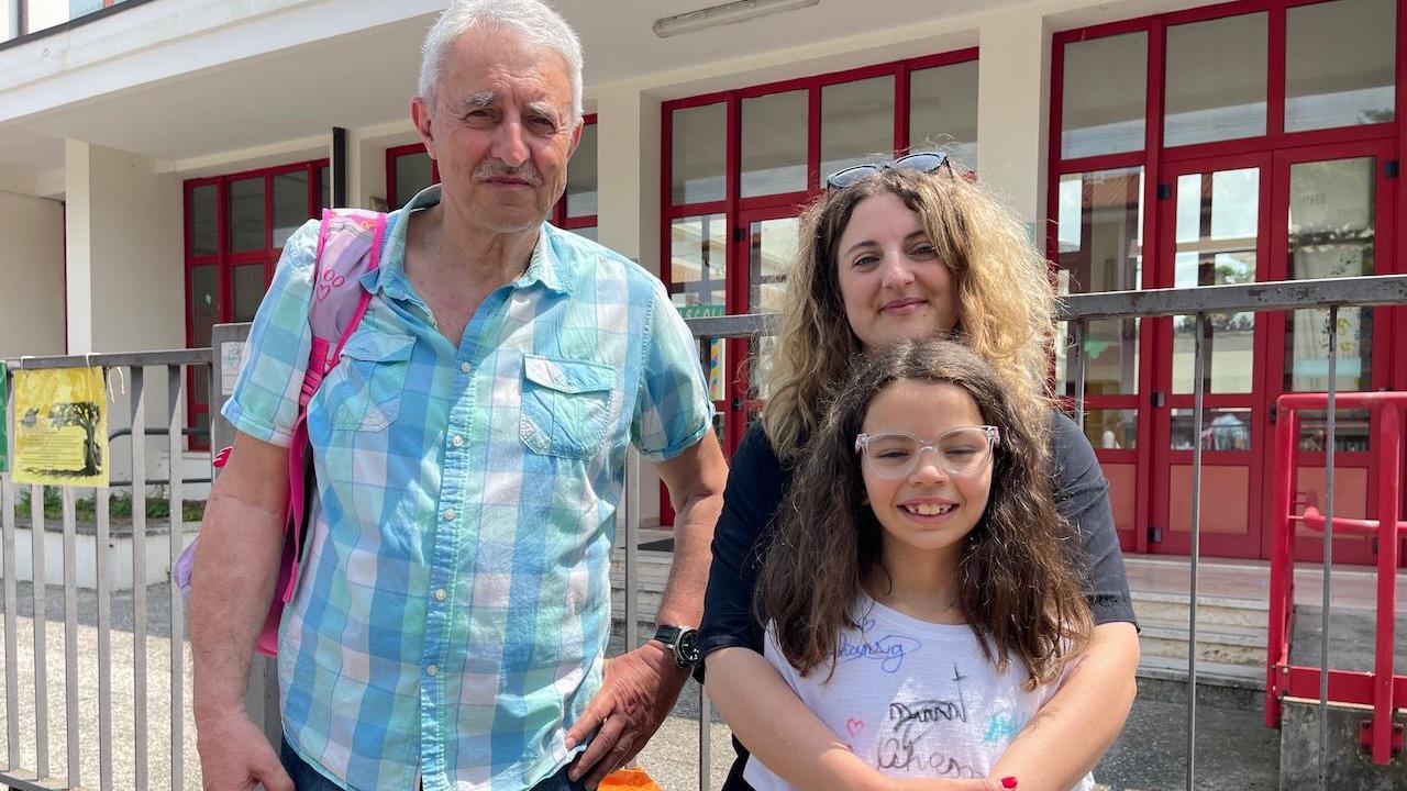 An older man, a mum and a daughter are seen in front of a building