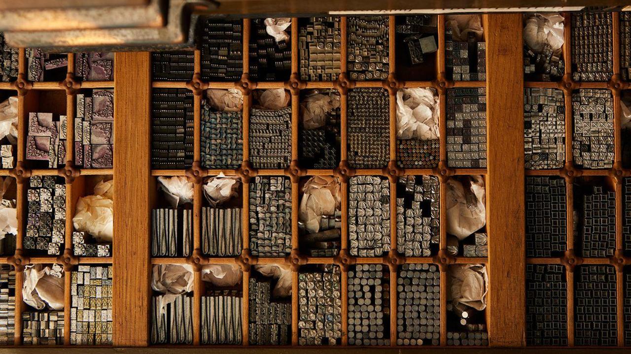 A wooden tray pictured from above, with lots of individual rectangular slots for metal stamps of symbols and letters.