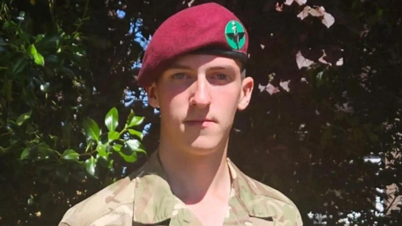 A soldier wearing a camouflage print shirt and a red beret with a green badge.