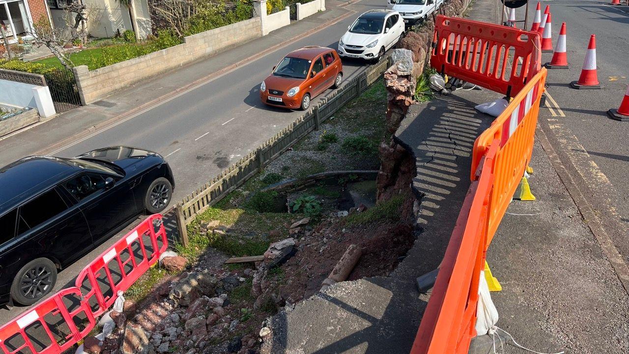 A view at the top of the collapsed wall shows it is between two roads and there are houses nearby.