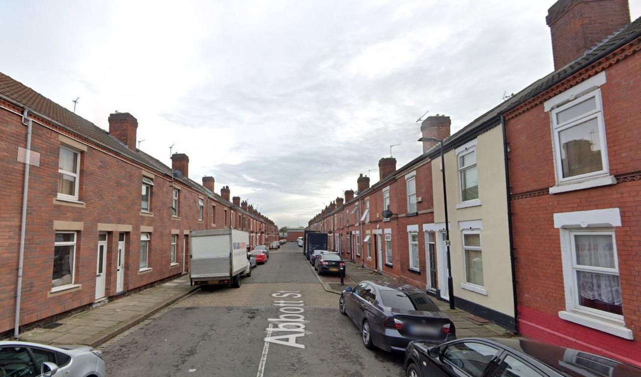 Row of red-brick terraced houses in Hexthorpe, Doncaster looking towards the train line. Several parked cars on both sides of the road and a white van parked on the left of the road. Google Streetview down the middle of the road.