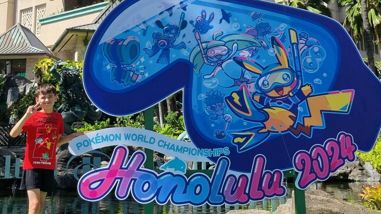 Declan poses with the Honolulu 2024 Pokémon World Championship signs 