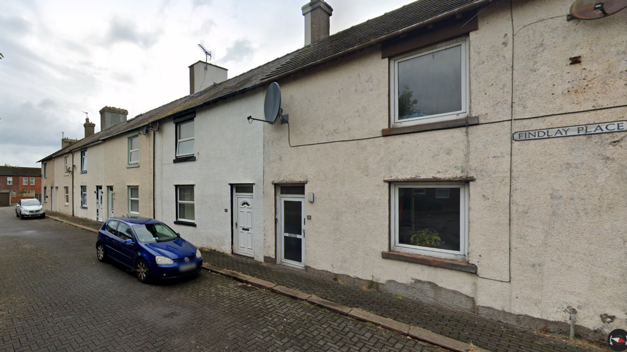 A row of older terraced housing painted cream and white with doors opening straight onto a pavement. In the distance you can see other brick buildings .