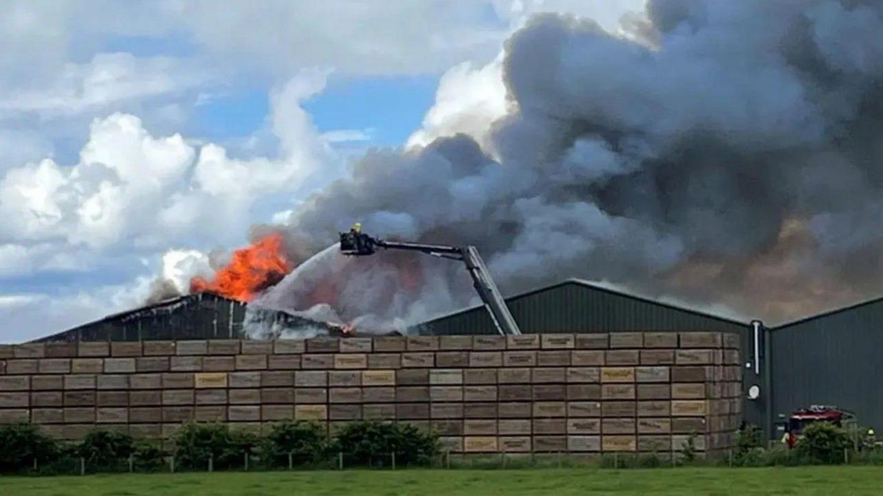 Luchd-smàlaidh a' dortadh uisge air togalach mòr air tuathanas ann an oidhrip cuir às dha teine