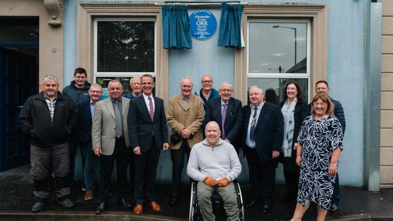 A group of people standing in front of the recently unveiled blue plaque for Alexander E Orr