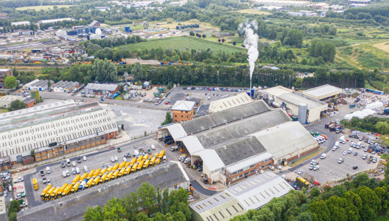 Aerial shot of Swindon's Waterside Park with various buildings, yellow lorries and a chimney with smoke emitting.