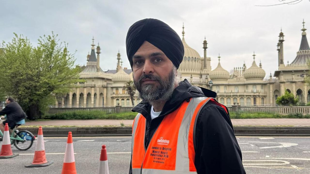 A man wearing an orange high-vis vest stood in front of the Brighton Pavilion