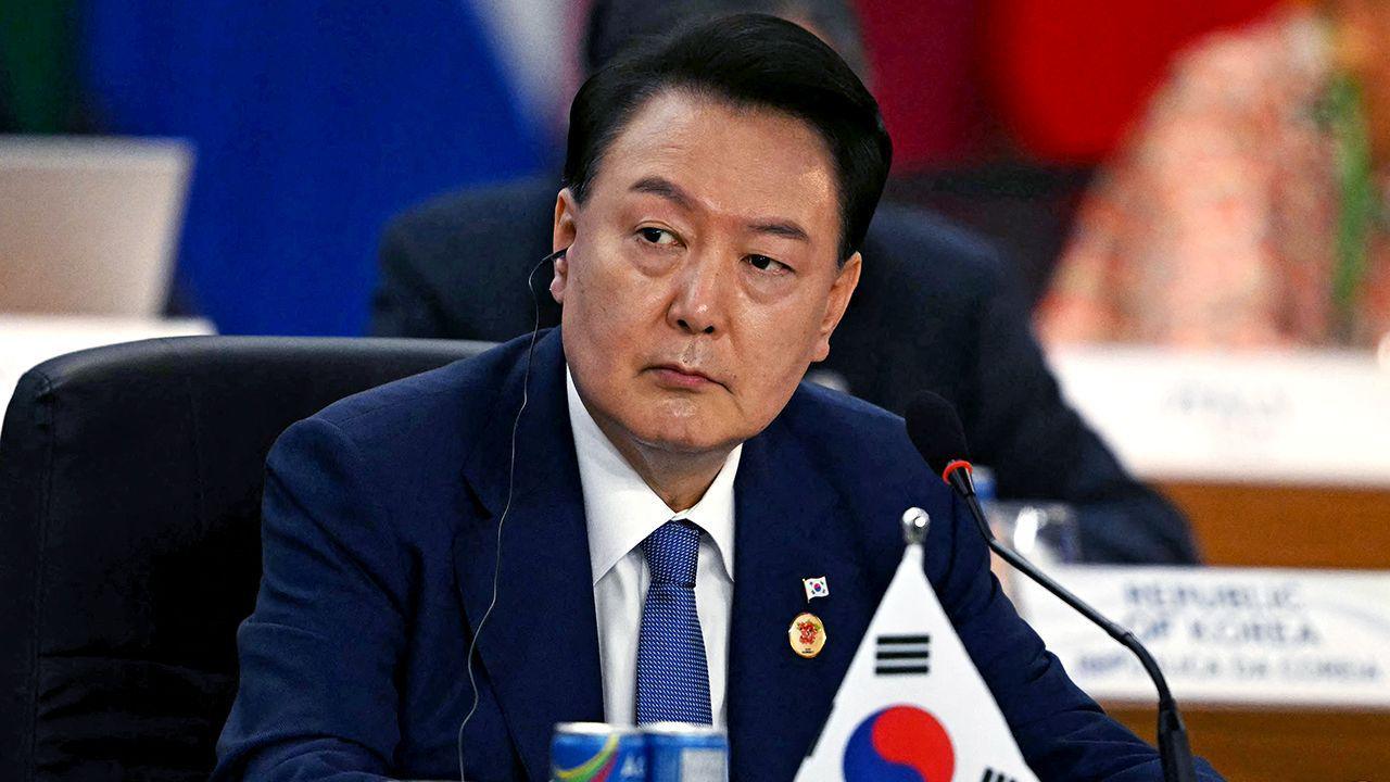 President Yoon Suk Yeol looks away from camera while wearing a suit and tie with an earpiece in, with a miniature South Korea flag and refreshments on the table in front of him as he sits during the third session of the G20 Leaders' Meeting in Rio de Janeiro, Brazil, on November 19, 2024.