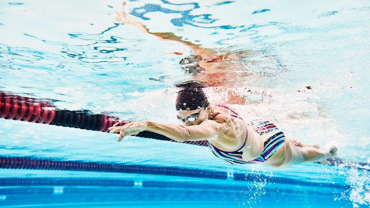 A woman wearing a swimming cap swimming in a swimming pool, seen from under the water level