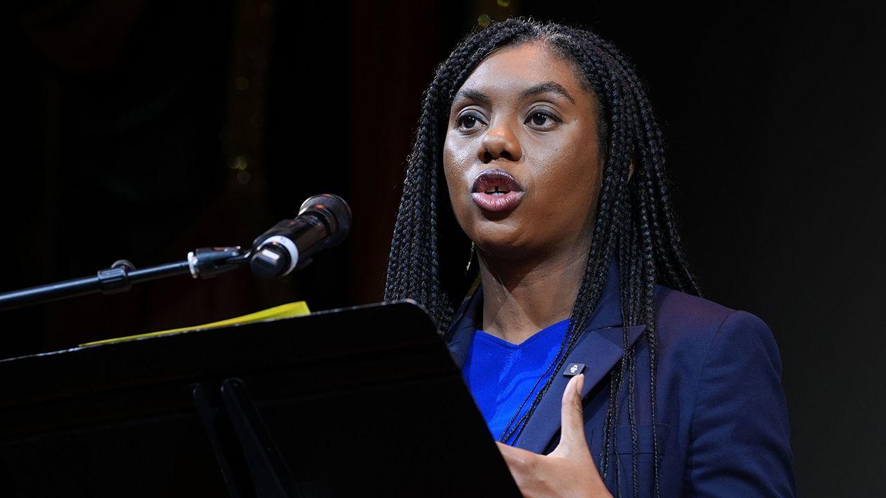 Conservative leader Kemi Badenoch, standing behind a black lectern on a stage, speaks to an audience