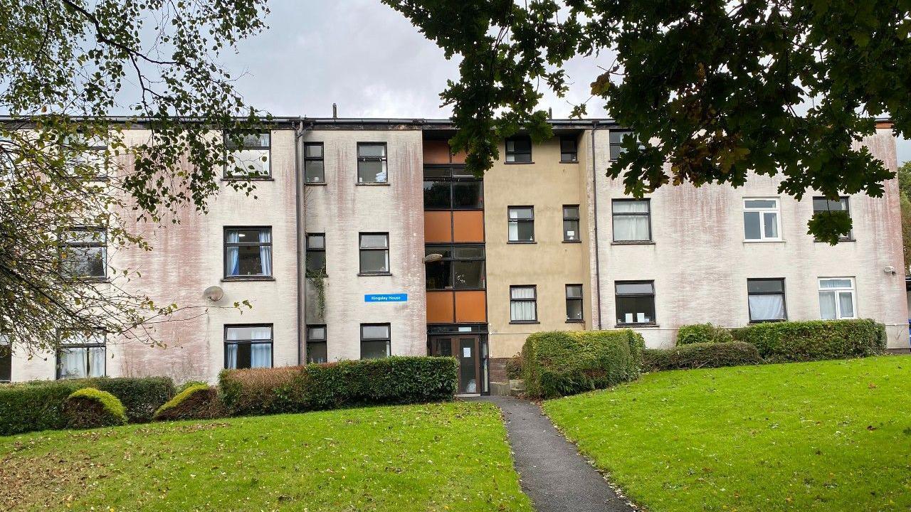 Three storey white accommodation block, with evident deterioration on exterior