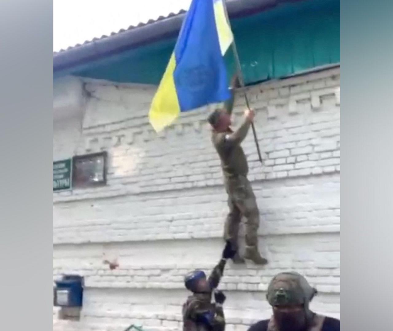 A still from footage shared on social media appears to show Ukrainian soldiers lifting their national flag while climbing a wall up to a tin roof of a building in Guevo, Kursk oblast on 11 August