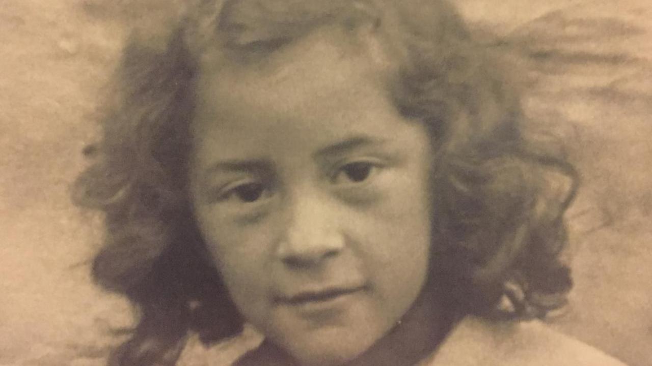 Sepia tone photograph of a young Māori girl with dark curly hair, wearing a cardigan.