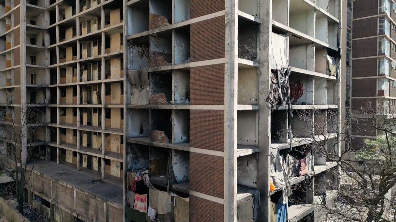A drone shot of the side of an abandoned building. The facade is covered in cloths providing protection for some of those living inside.