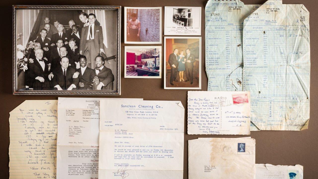 A picture of a number of letters on a table. They are pictured to the bottom of the image and spread out to the right side. In the top left corner, there are five photographs.