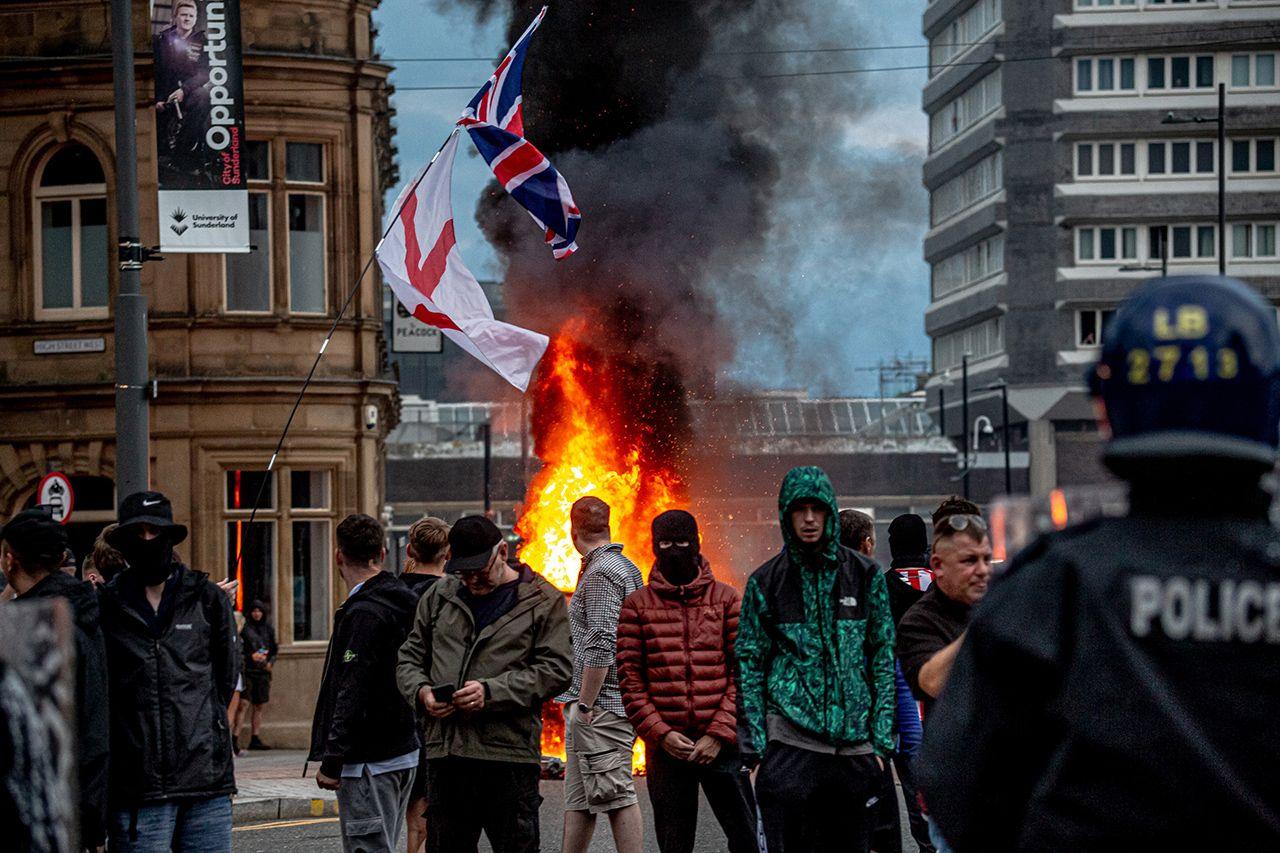 Anti-immigration protesters gather in front of a burning Citizens Advice bureau 