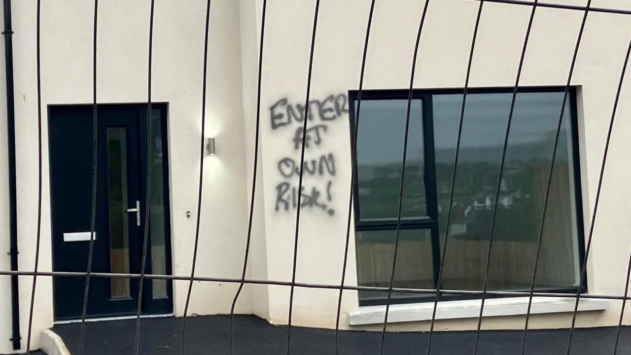 A house with the words 'Enter At Own Risk!' spray painted near the front window of the property.