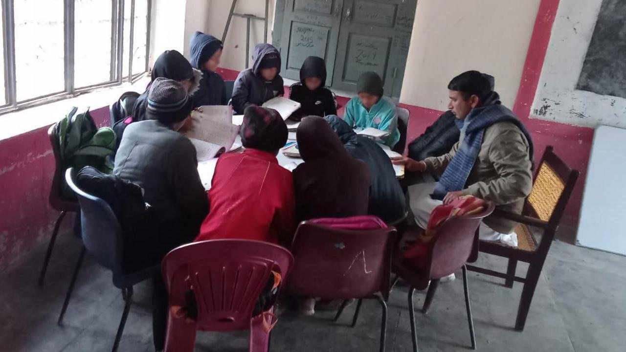 Eleven pupils sit around a large circular desk with their teacher.