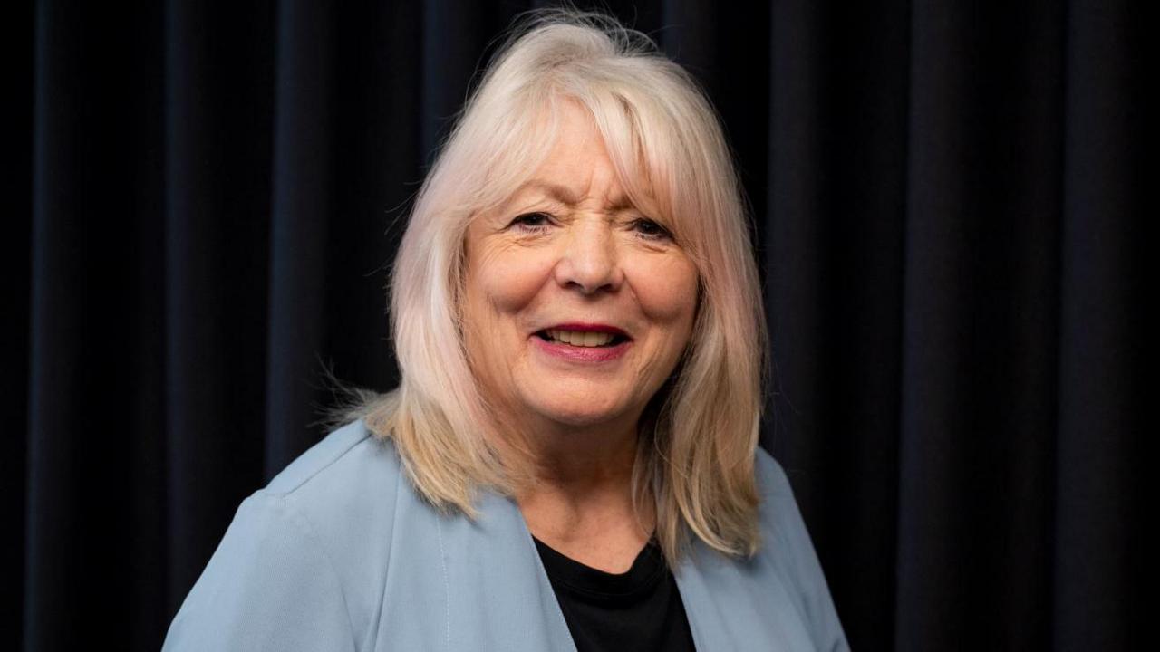 A close up shot of actress Alison Steadman looking to camera with a black background