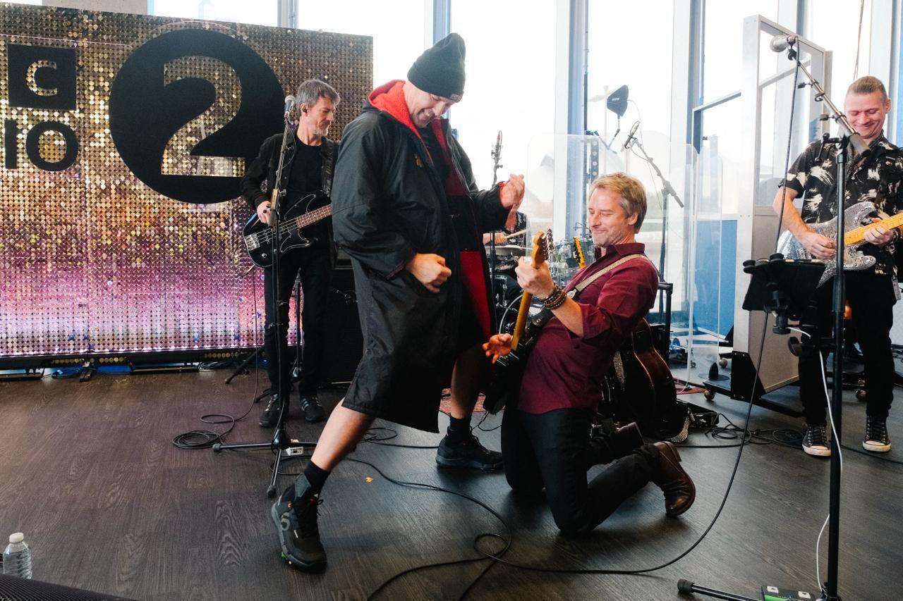 Paddy McGuinness on stage playing air guitar as Chesney Hawkes, on his knees plays guitar with band in background