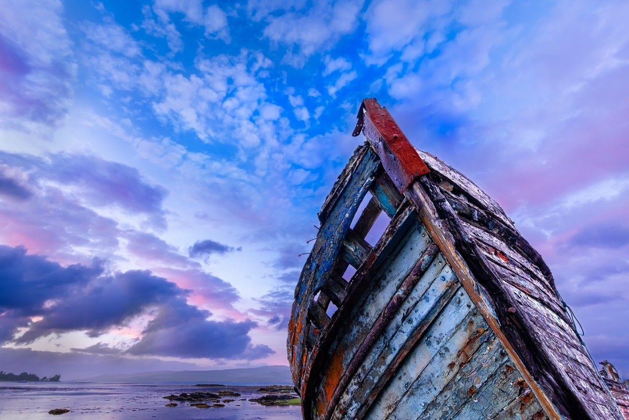 A shipwrecked boat, with a sky of blues, pinks and purples above it